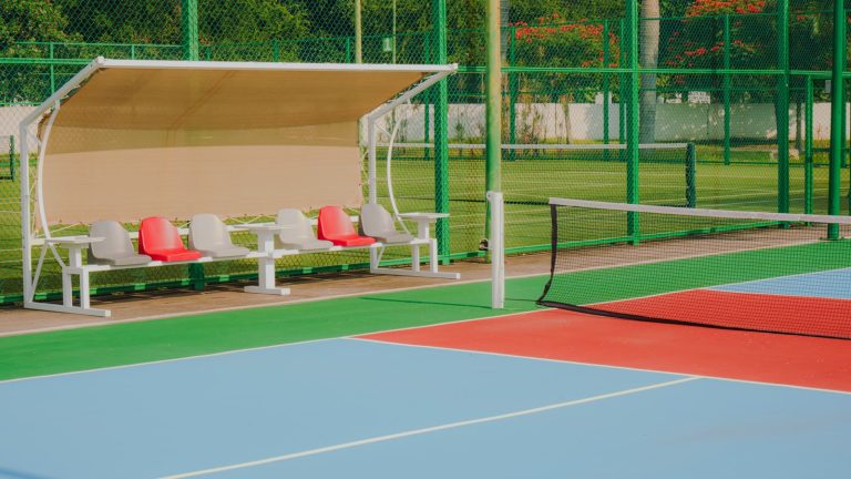 Tom overdækket spillerbænk med tomme sæder ved en blå og rød tennisbane