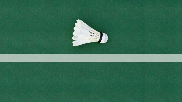 Fjerbold liggende på en grøn badmintonbane ved en hvid banelinje