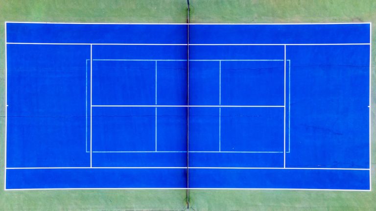 Blå hardcourt-tennisbane set lige oppefra med hvide banelinjer og nettet ned gennem midten