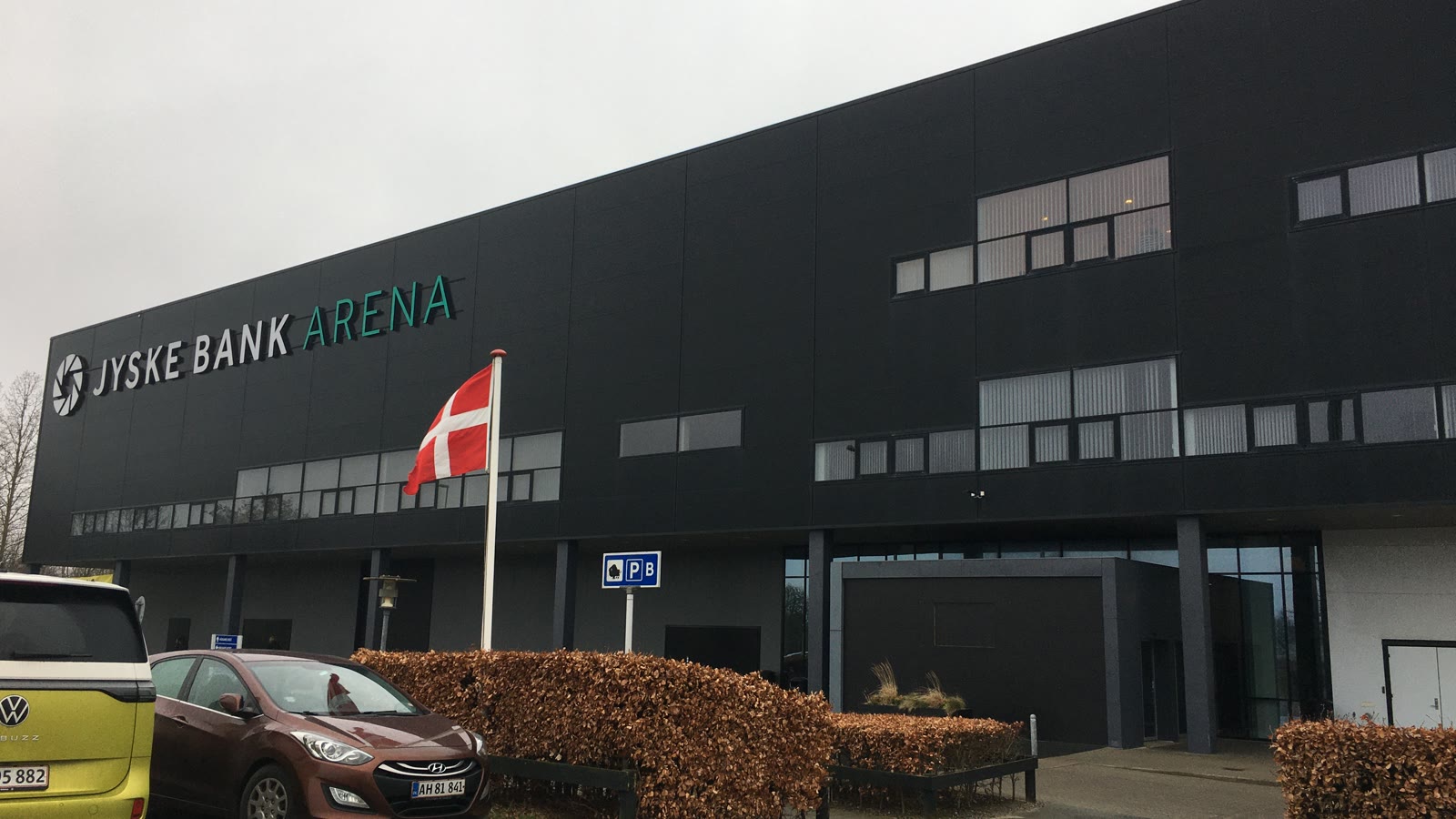 Facaden på arenaen i Odense med det tidligere navn Jyske Bank Arena og et dansk flag foran indgangen