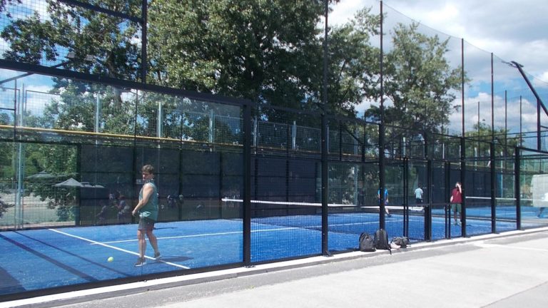 Padelspillere på to udendørs baner med blåt kunstgræs bag glasvægge