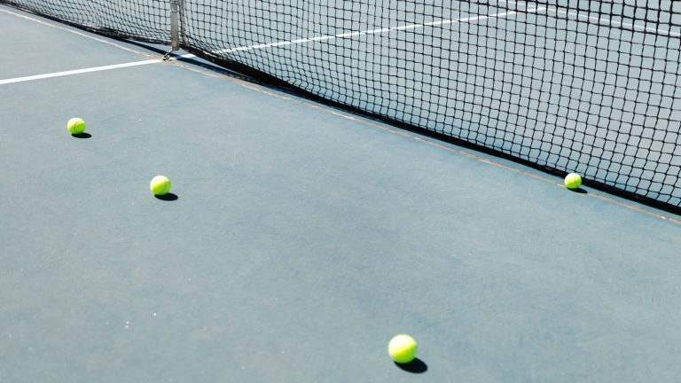 Fire tennisbolde spredt på en blå hardcourt-bane ved nettet i sollys