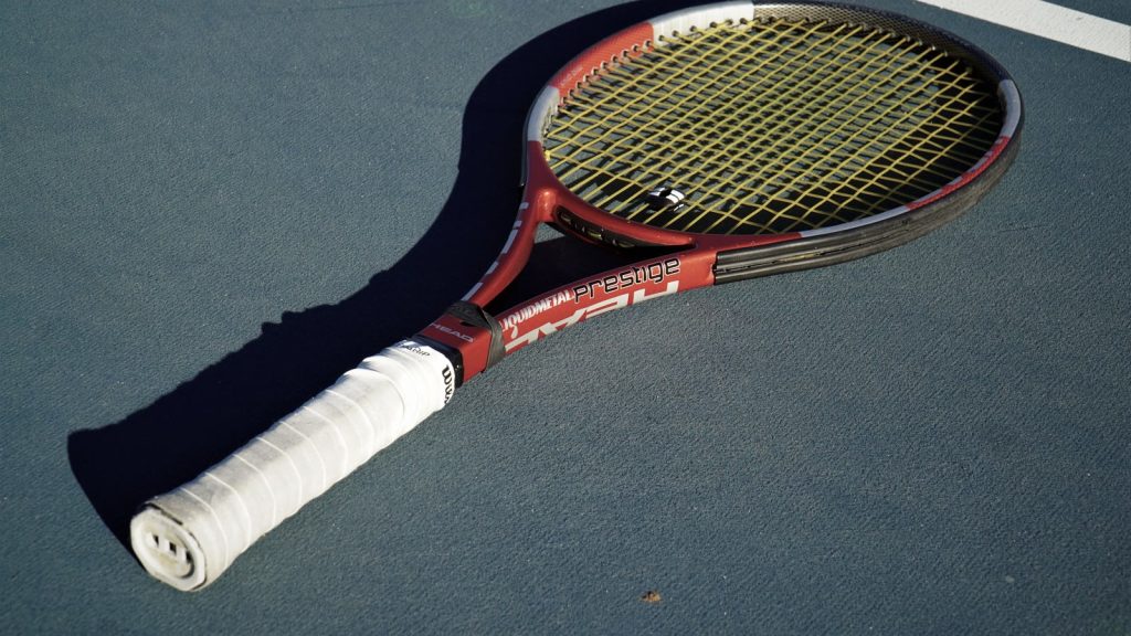 Rød og hvid tennisketcher med hvidt greb ligger alene på en blå hardcourt-bane i lavt sollys